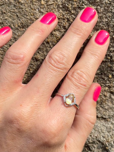Hand wearing a ring with a diamond shaped cintrine gemstone against a textured background 