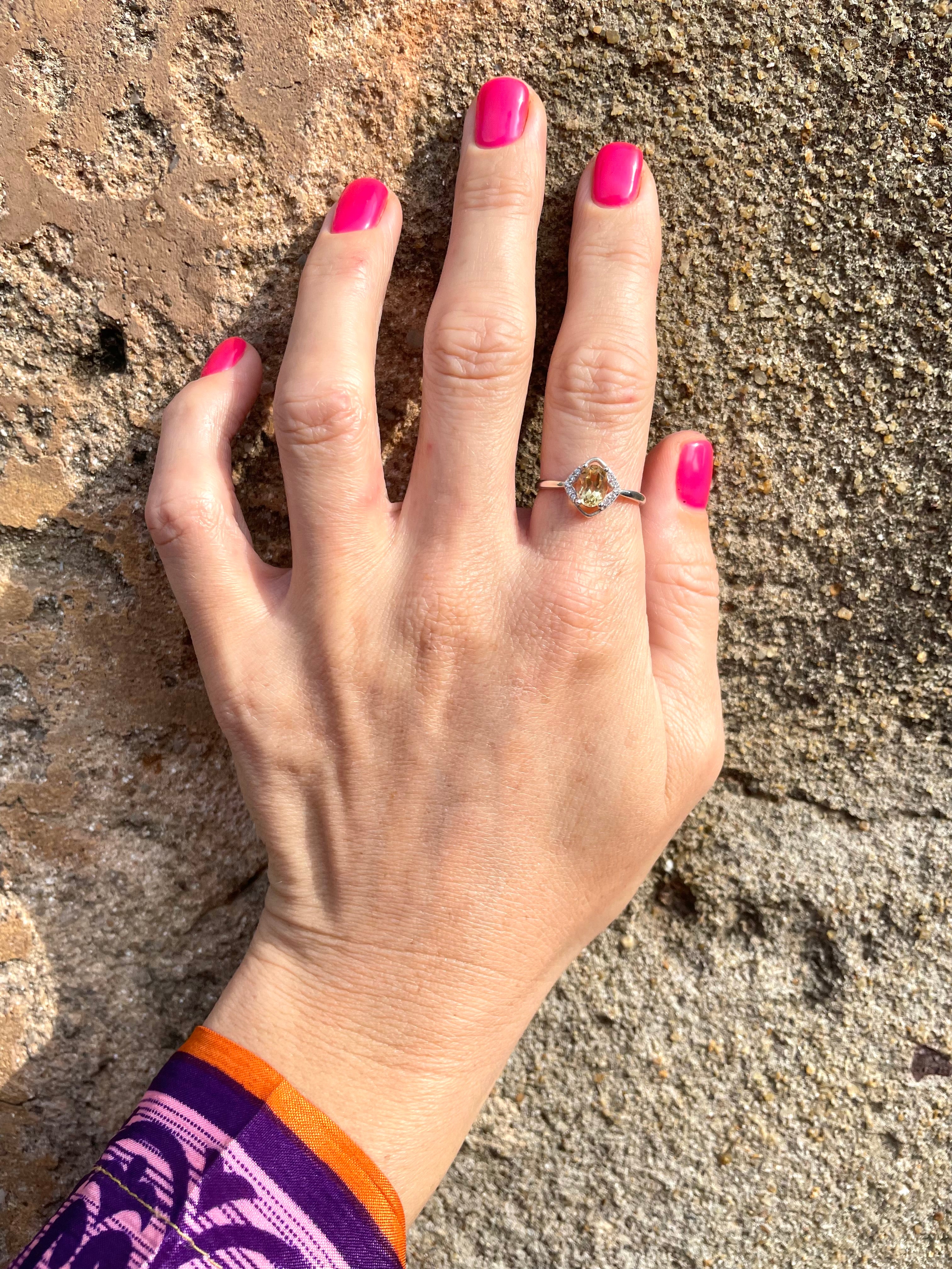Hand with pink nail polish wearing a diamond shaped Cintrine gemstone and silver ring against a big rock in Sri Lanka