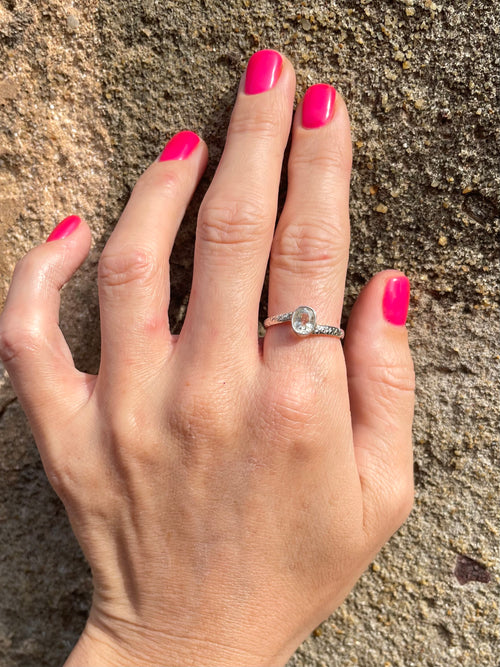 Hand with pink nail polish wearing Sri Lankan white sapphire stone in engraved silver band 