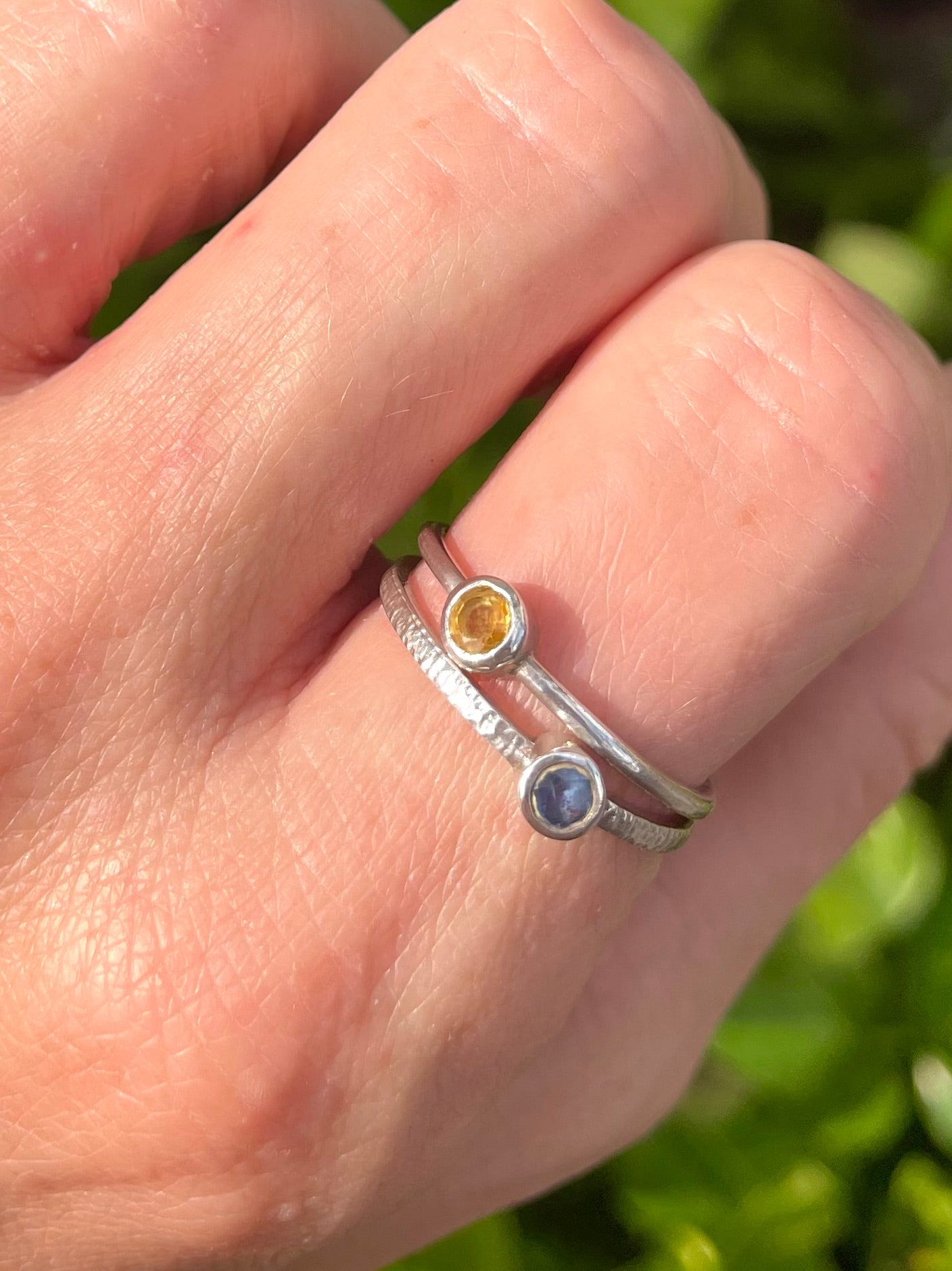 Hand wearing two silver rings with petite sri lankan sapphires against a leafy background