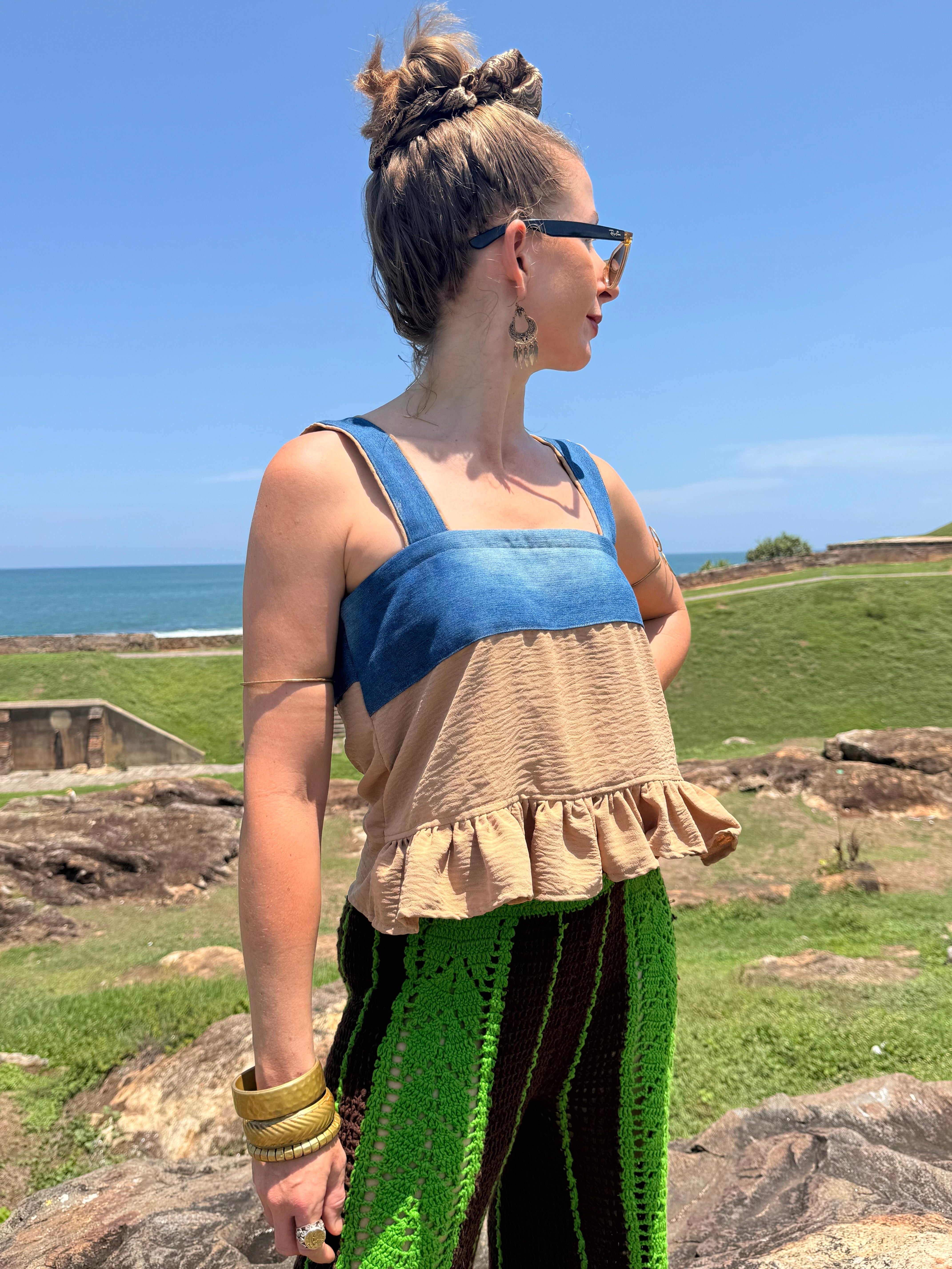 Woman standing outdoors with a scenic background of ocean and sky in Sri Lanka wearing retro baby doll top made from recycled denim jeans and khaki pants