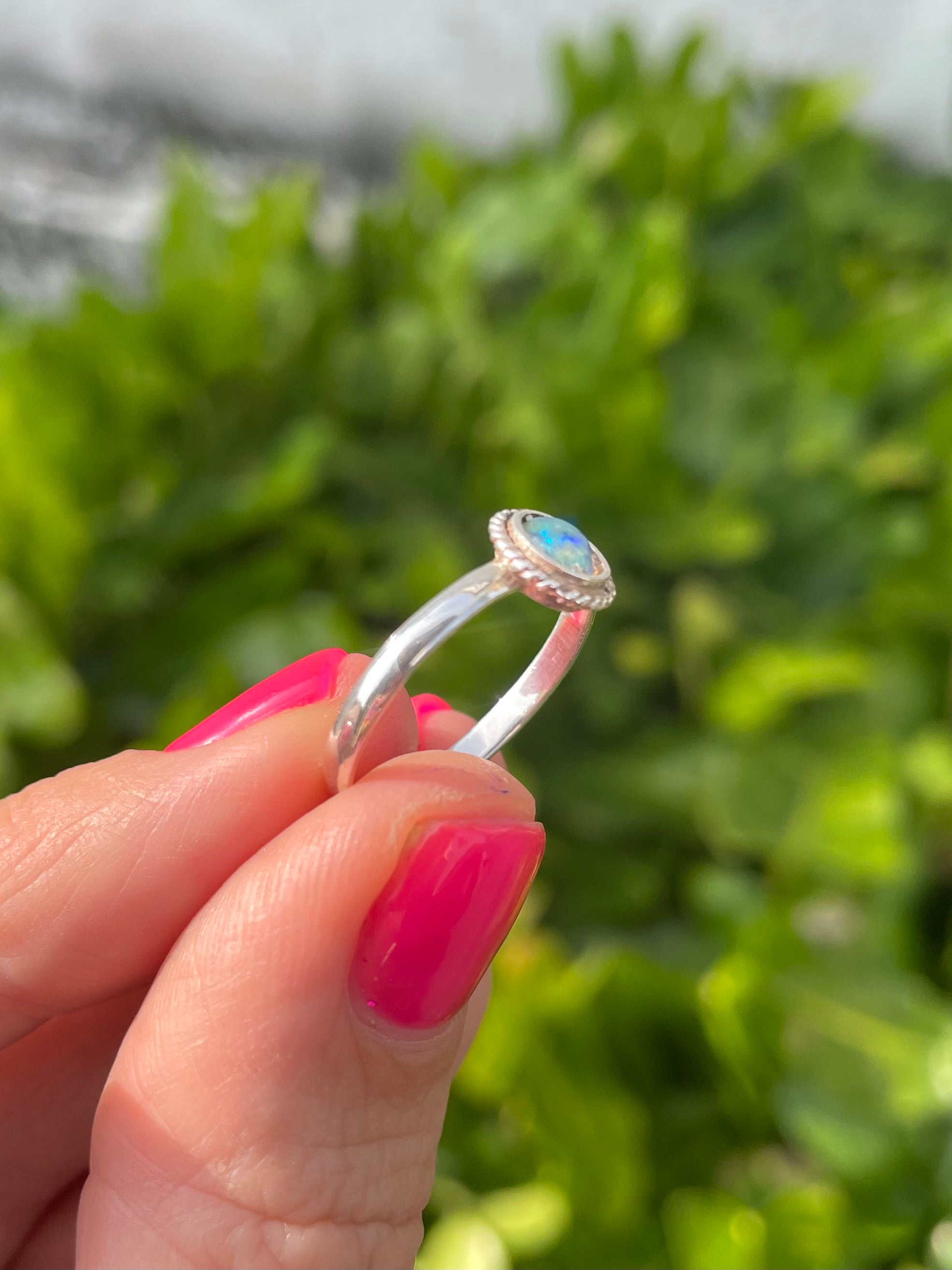 Silver ring with a opal held by a hand against a blurred green background