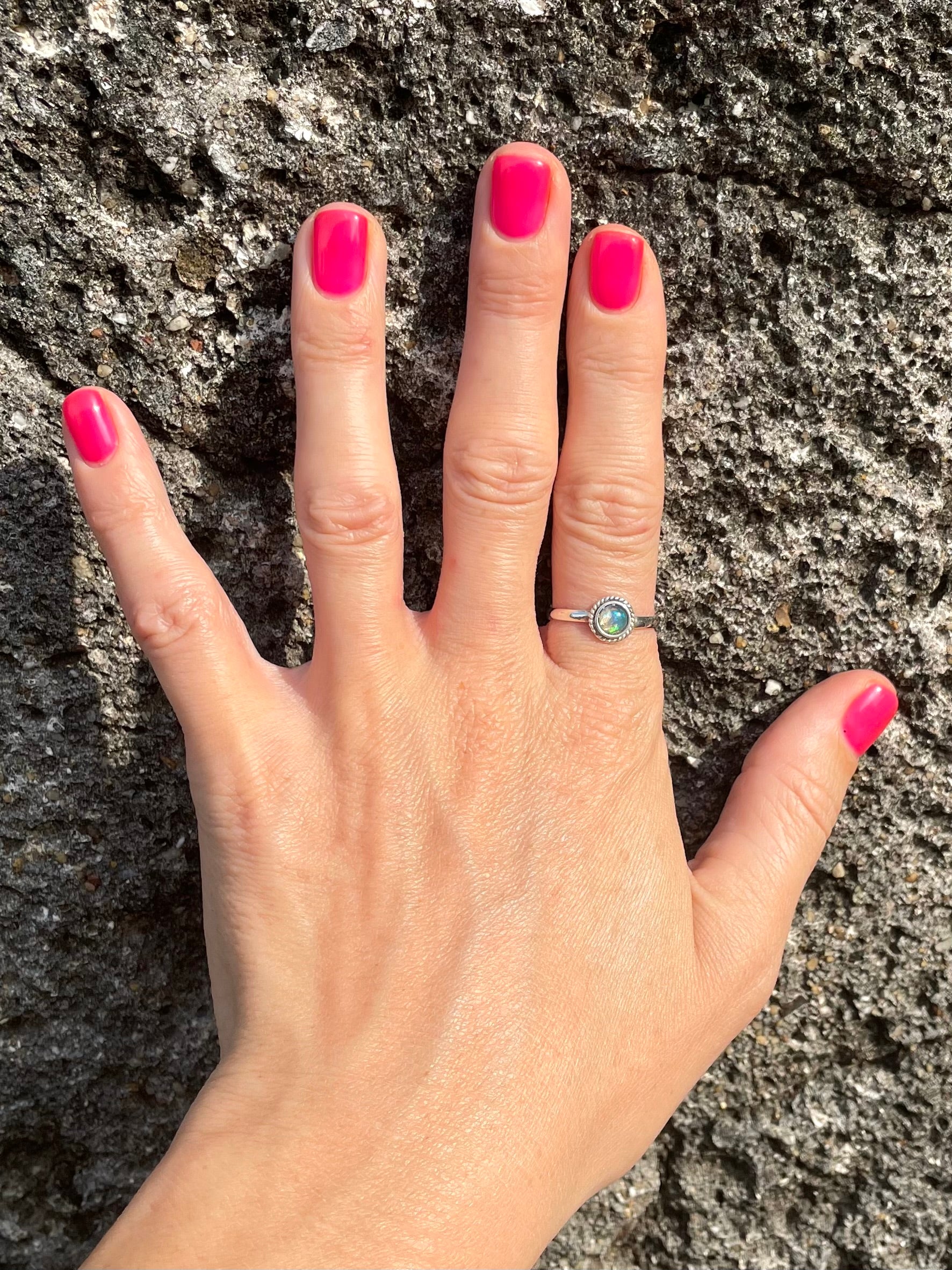 Hand with pink nail polish wearing a silver ring with a green gemstone against a rock