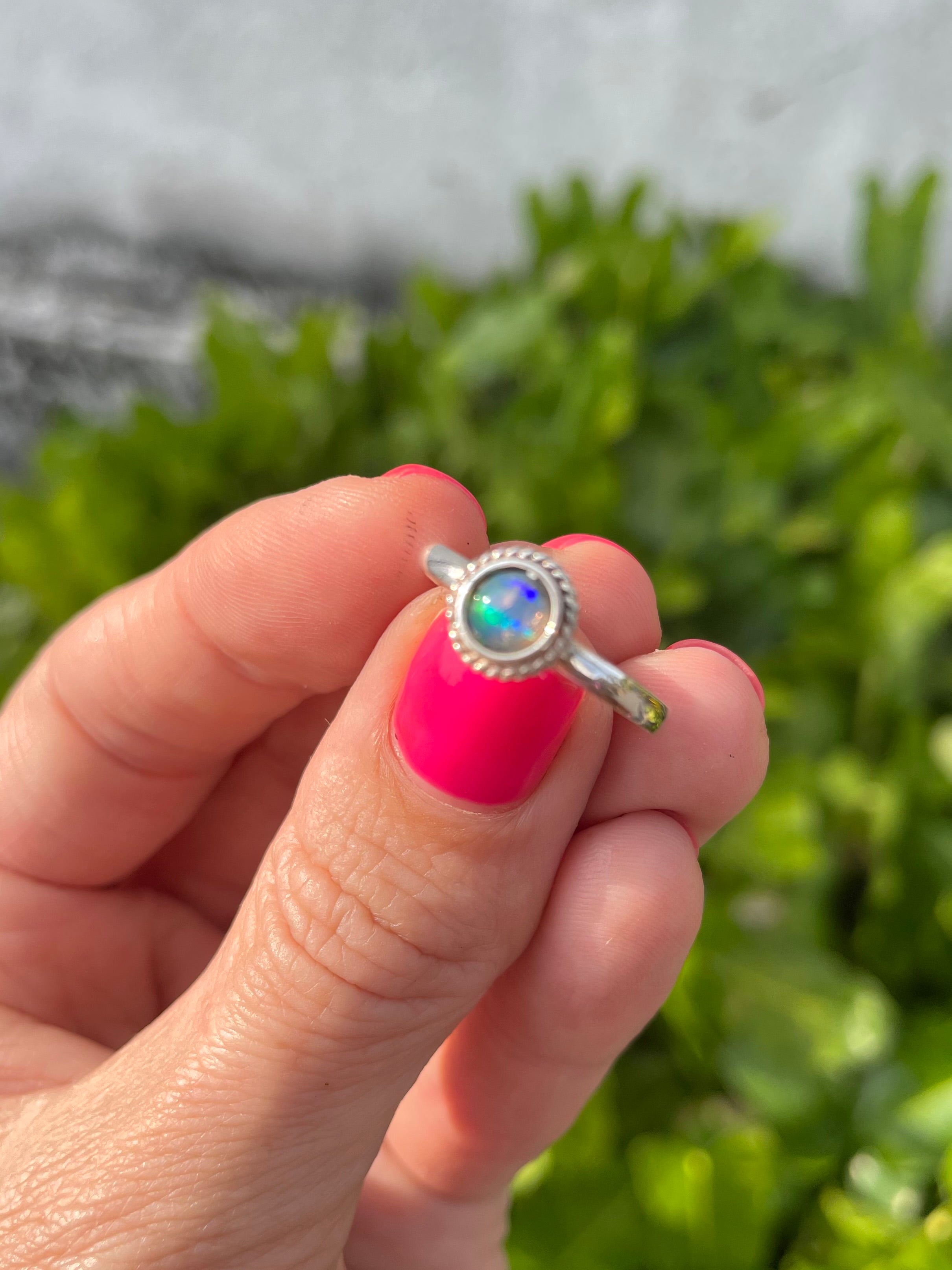 Silver ring with a colorful opal gemstone held by a hand against a blurred green background