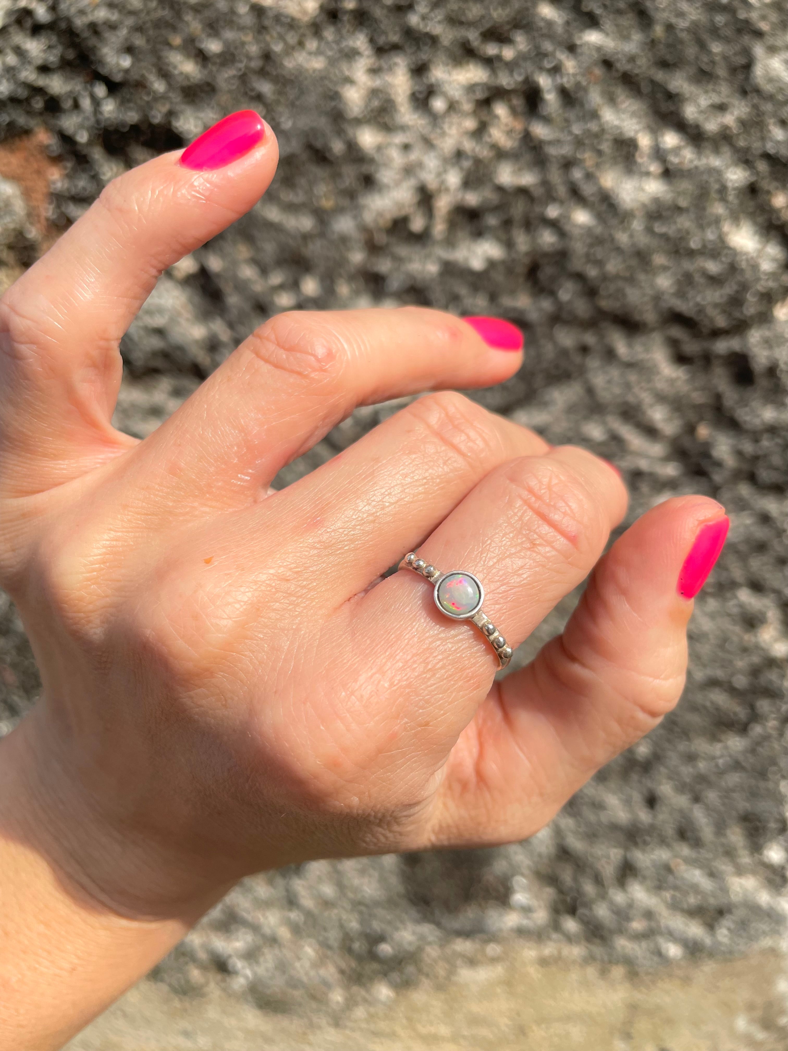 Hand with pink nail polish wearing a silver ring with Sri Lankan opal, textured background