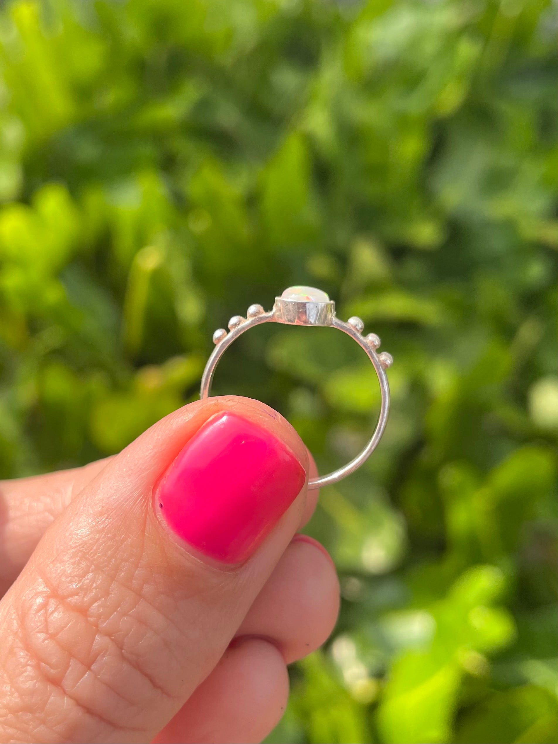 Silver ring held by a hand with pink nail polish against a green leafy background